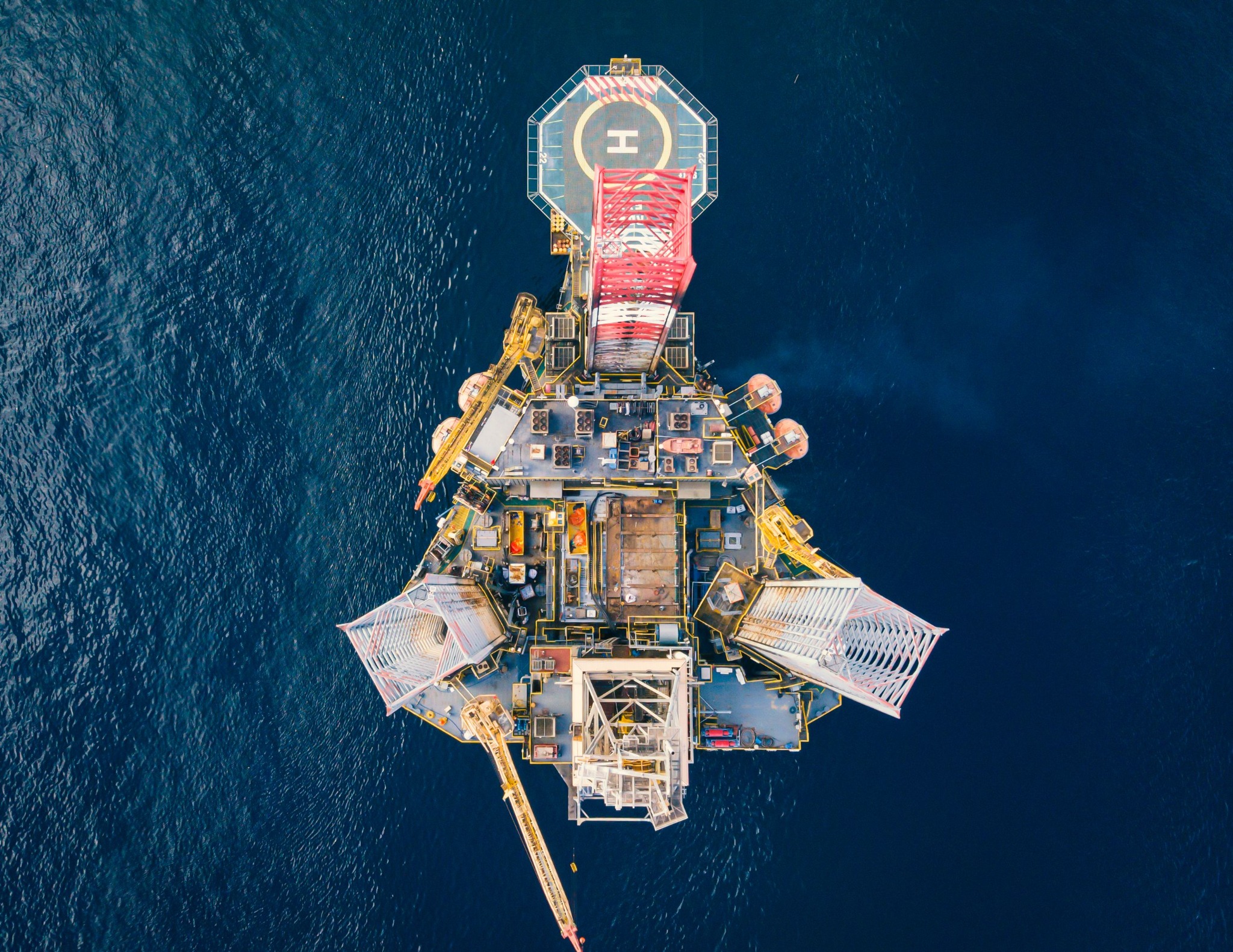 Aerial view of an offshore oil and gas platform with a helipad surrounded by blue ocean